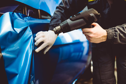 A person using a heat gun to carefully apply a vinyl car wrap, ensuring a smooth and durable finish.