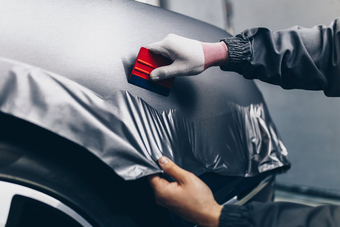 Car wrapping specialist applying vinyl foil to a vehicle, showcasing detailed craftsmanship with a focus on precision.